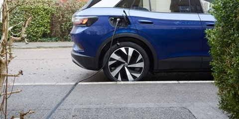 Photo showing an EV with a charging cable running through a pavement.