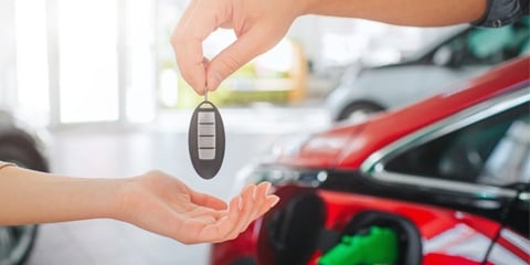 Photo of EV keys being handed over with an EV charging in the background